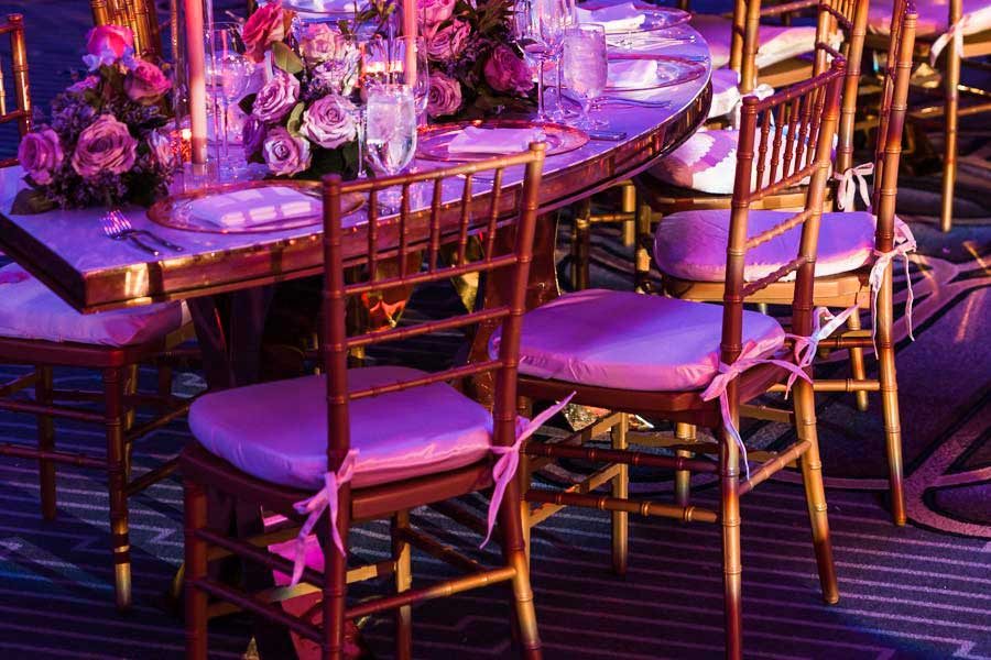Gold Chiavari chairs with pink cushions at a table with purple floral arrangements and candles.
