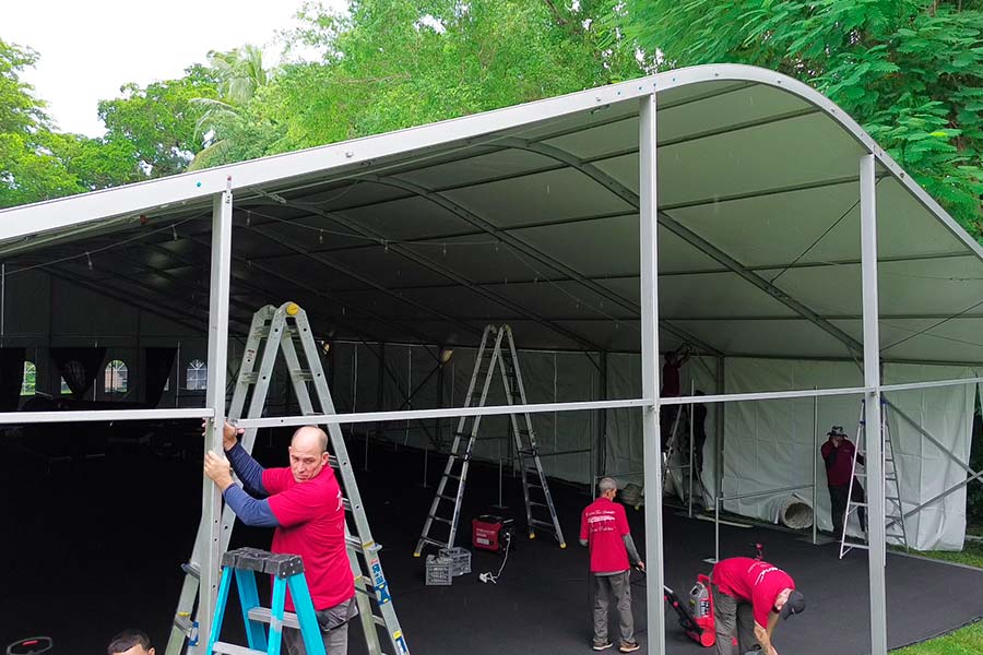 Event crew assembling the aluminum structural frame of a large commercial marquee tent outdoors.