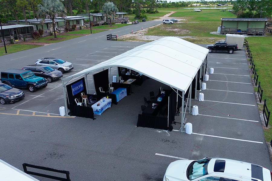 High-angle view of a white commercial event tent set up in a parking lot with black pipe and drape partitions.