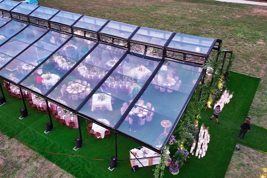 Overhead view of a luxury clear wedding tent featuring green turf flooring and elegant dinner seating.