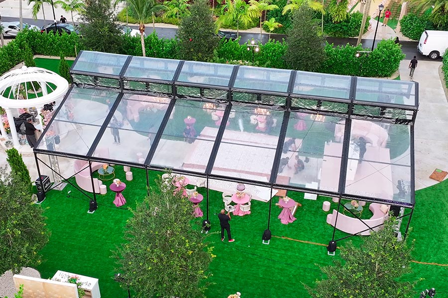 Luxury clear top wedding tent with pink lounge furniture and dance floor on green turf.