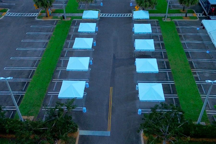 Row of white pop-up canopy tents secured with blue weight bags in a parking lot.