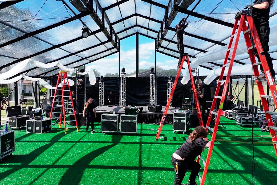 Technicians installing professional stage lighting and rigging inside a clear-span event tent.