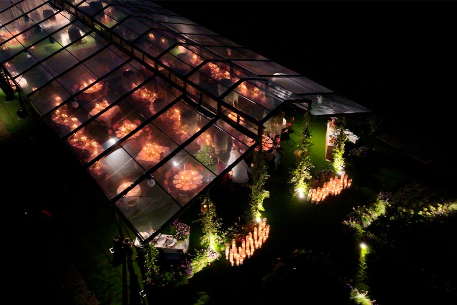 Nighttime high-angle shot of a transparent wedding marquee filled with candlelit tables and guests.
