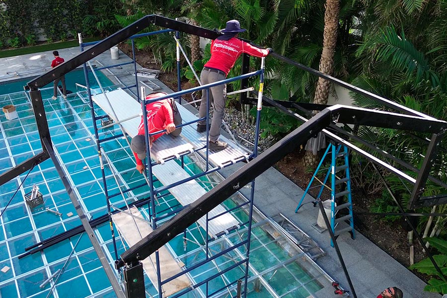 Construction workers on scaffolding installing a custom glass floor over a swimming pool for an event.