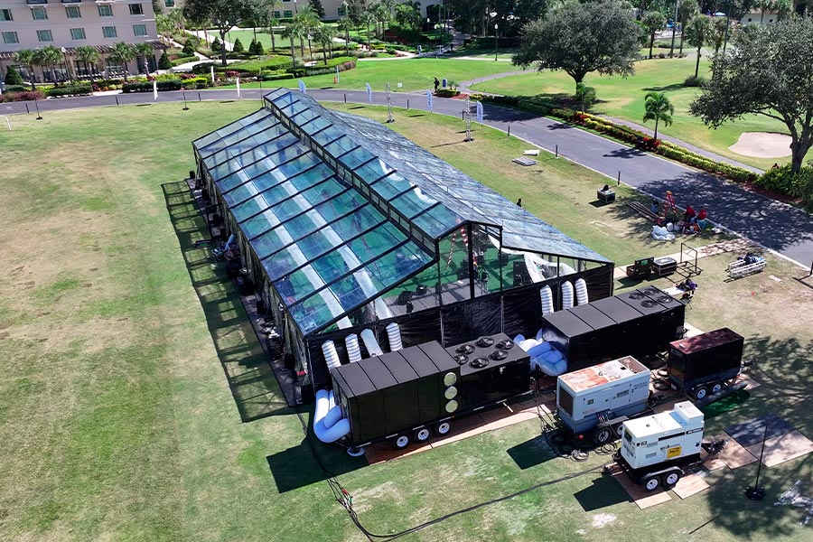 Aerial view of a large clear-top event tent with industrial HVAC units and power generators.