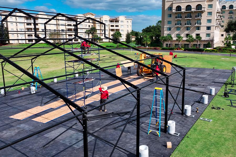 Crew assembling a black large-scale event tent frame on a modular flooring system at a resort.