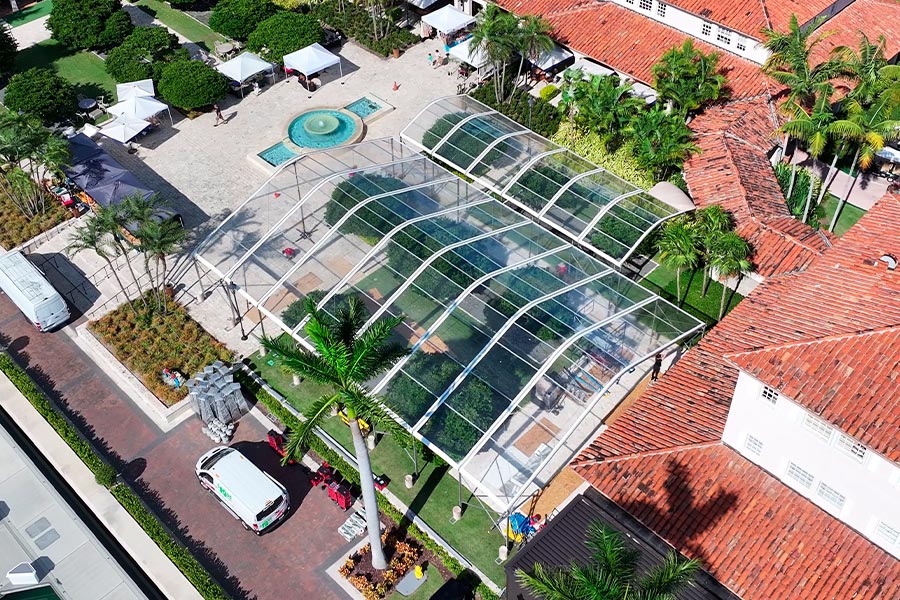 Modern curved clear frame wedding tents arranged in a courtyard near a fountain and palms.