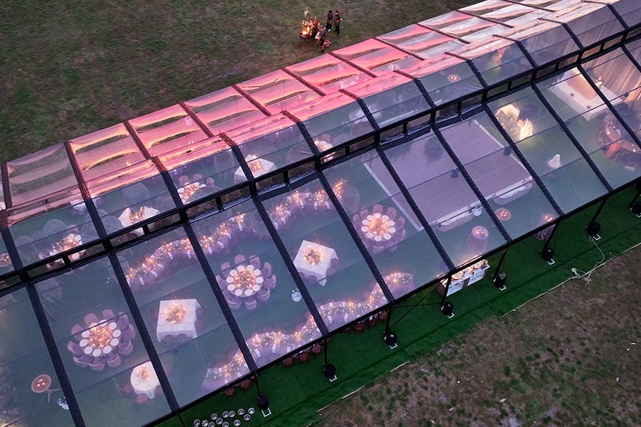 Illuminated clear-span wedding tent at twilight featuring glowing centerpieces and a dance floor.