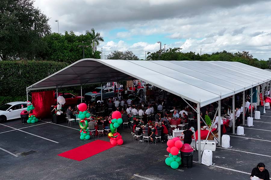 Outdoor event tent with red carpet entrance, festive balloon pillars, and guests seated at round tables.