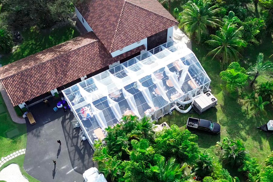 High-angle shot of a transparent marquee tent with white fabric draping connected to a classic tile-roof venue.