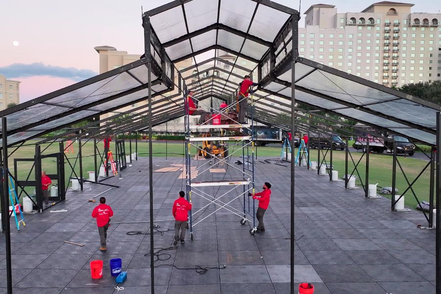 Crew installing clear roof panels on a large wedding tent structure during sunset.
