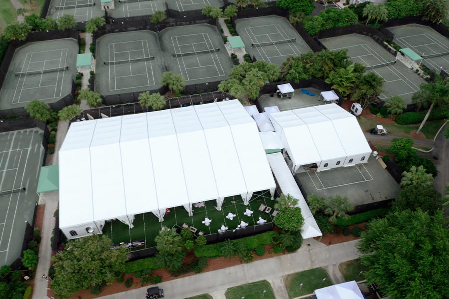 Large white gabled event tents connected by walkways on a green outdoor sports complex.