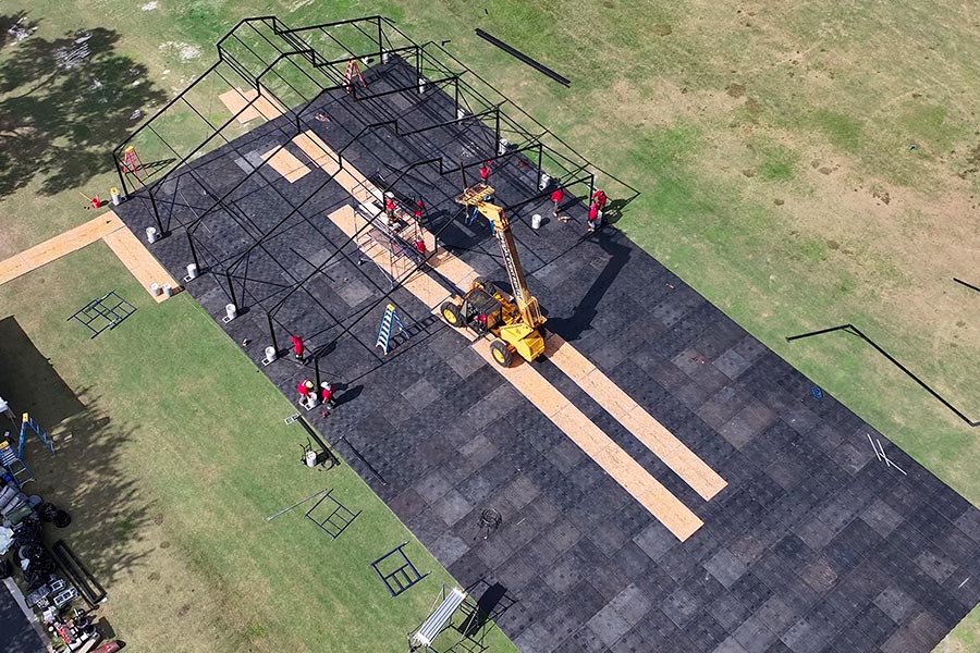 Professional crew installing a large black frame event tent on a protective subflooring system.