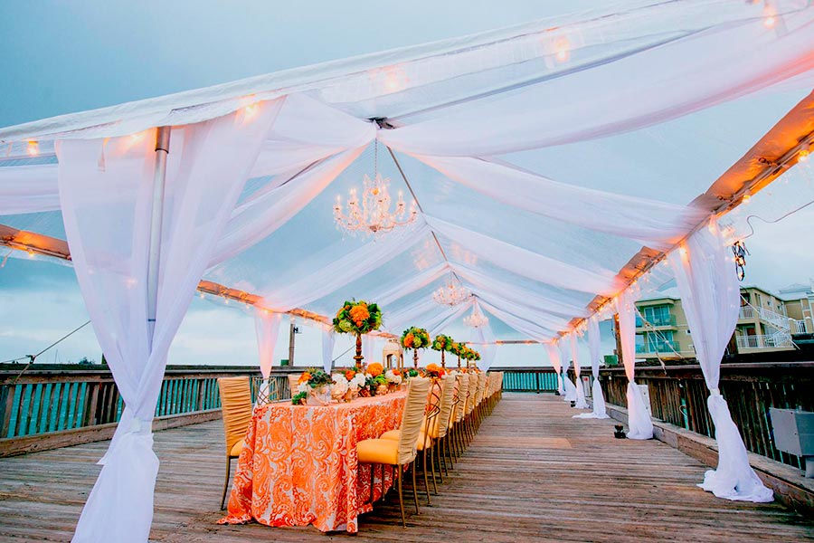 Elegant wedding party tent with white draping, chandeliers, and long banquet tables.