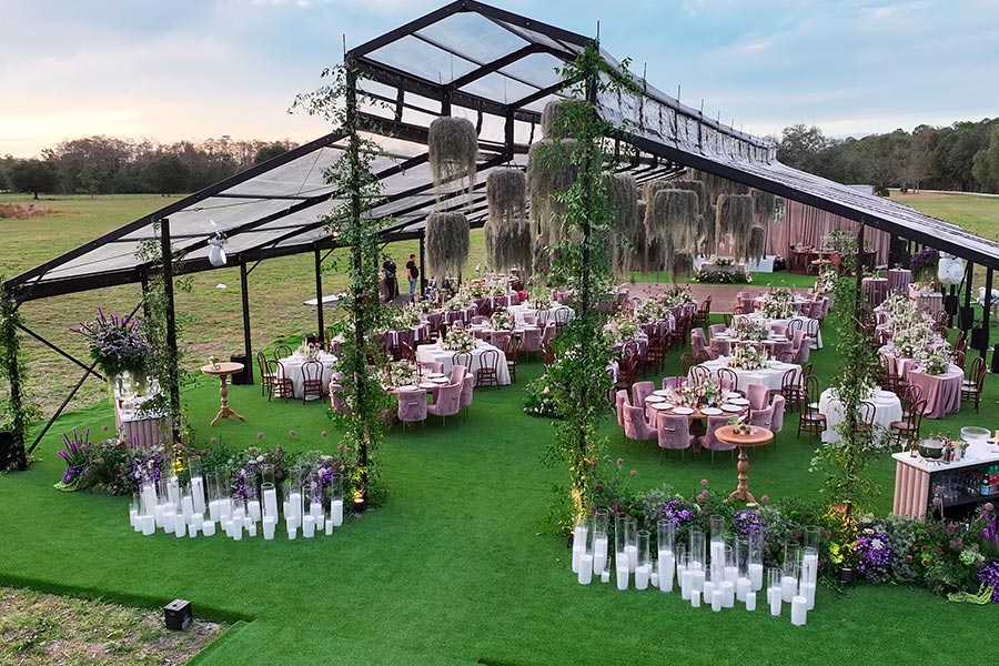 Elegant clear-top party tent with hanging greenery, floral arrangements, and round tables on green turf.