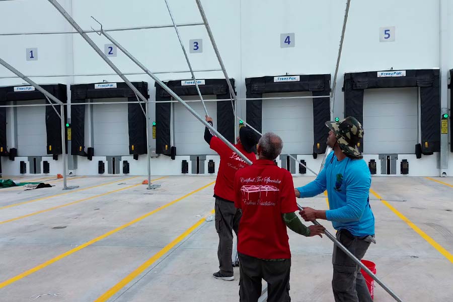 Professional tent installation crew in red shirts assembling a metal frame structure at a warehouse loading dock.