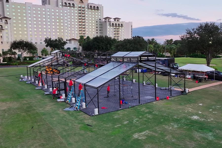 Professional crew installing a large black-frame clear wedding tent on a green lawn for a spring event.