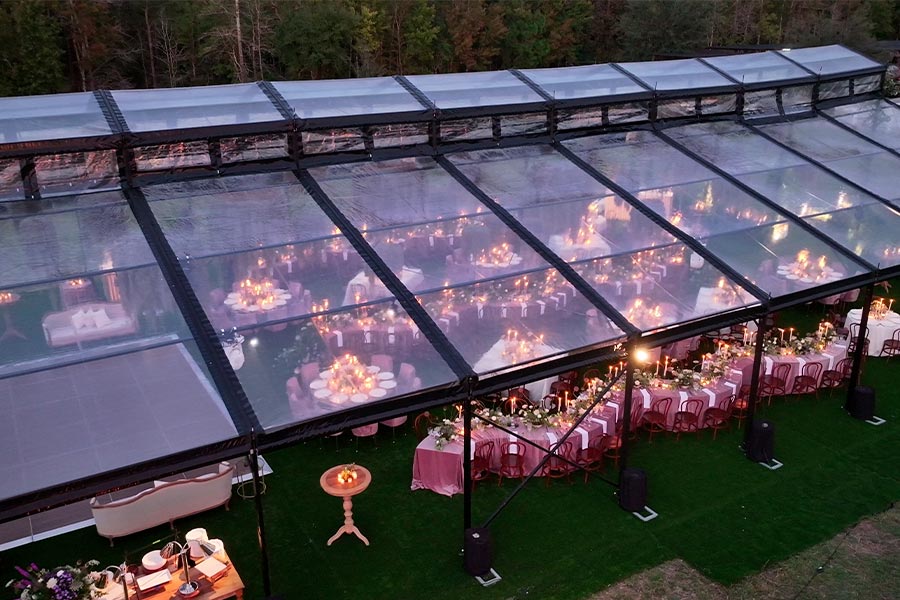 Interior view of a clear wedding tent featuring long banquet tables, pink linens, and romantic candlelight.