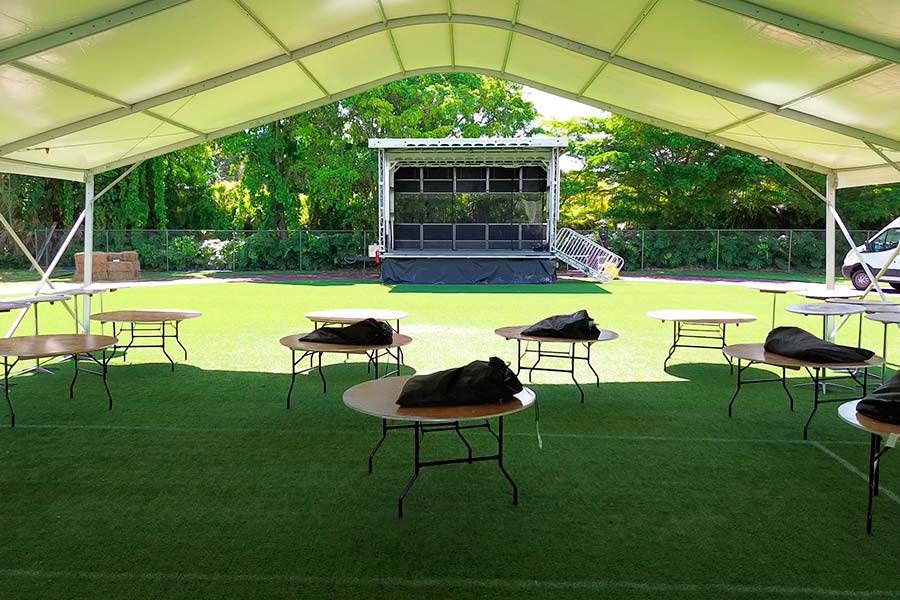 Event tent interior with stage setup and round tables on artificial grass; outdoor concert or party venue rental.