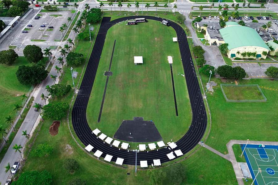Aerial view of a high school track and field with white event tents set up on the infield grass for seating.