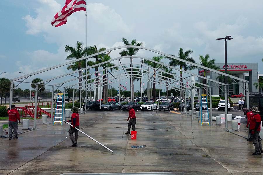 Installation crew setting up a large, commercial tent frame in a car dealership parking lot, below a Toyota sign.
