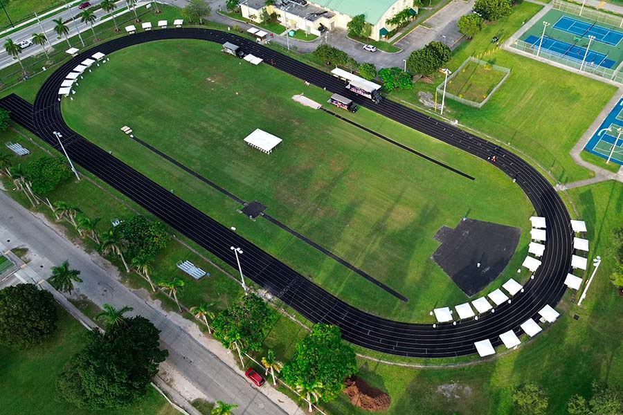 Drone view of a large sports field with a running track surrounded by multiple white event tents for shade or seating.