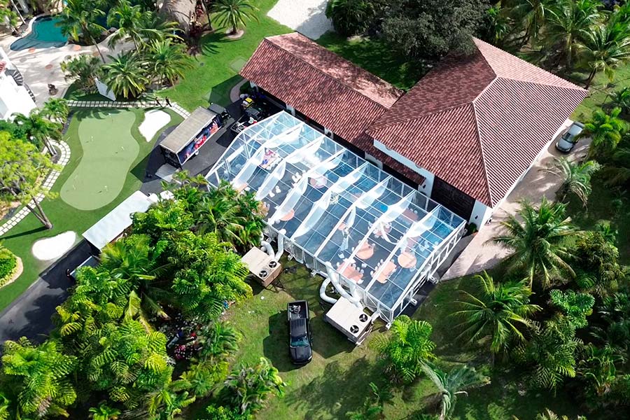Aerial view of a clear-top tent banquet style setup next to a Mediterranean-style home and putting green.