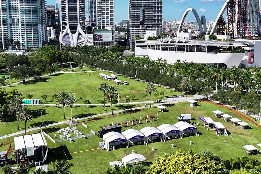 Aerial view of a white event tent setup on a green lawn near the Barry University campus sign.