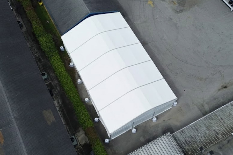 Overhead view of a long white event tent with a curved roof structure set up on a paved surface for an occasion.