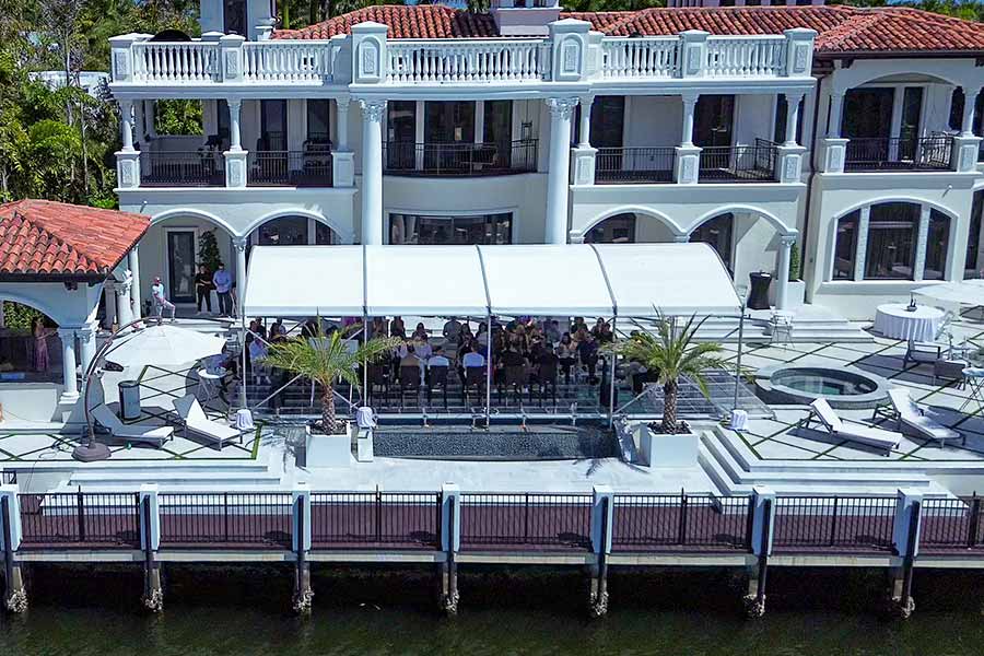 White event tent set up over a small pool on the patio of a large mansion for a business presentation.