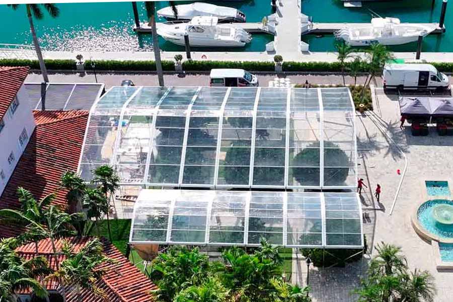 Aerial shot of a clear roof event tent installation near a resort-style pool and marina with boats.
