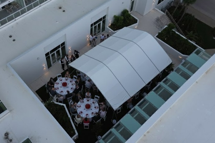 Aerial view of a white curved-roof outdoor event tent set up on a rooftop patio with round dinner tables.
