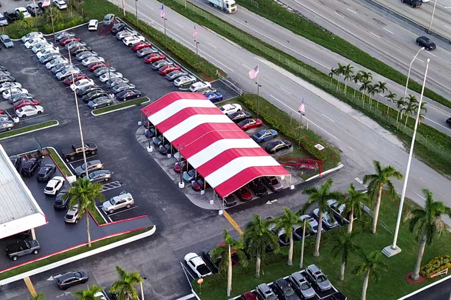 High-angle view of a red and white striped tent used for a corporate car sale event at a dealership lot.