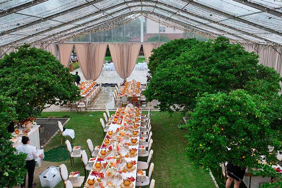 Interior of a clear tent with string lights and two long banquet tables set for a garden party.