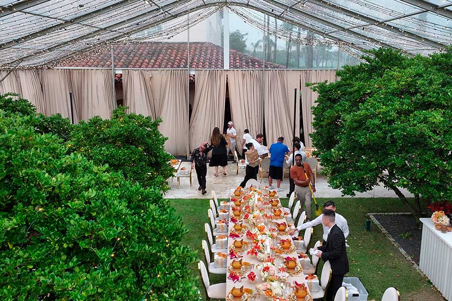 Catering staff setting up an outdoor wedding reception under a clear frame tent with draping.