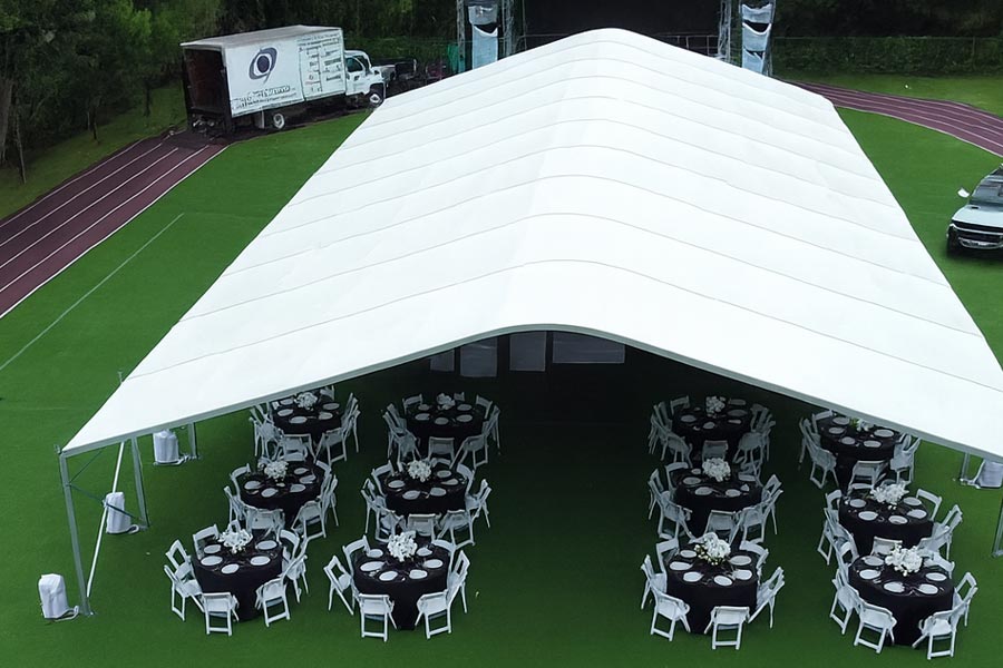 Elevated view of a large white tent on an artificial turf field, set with black tables for family dining.