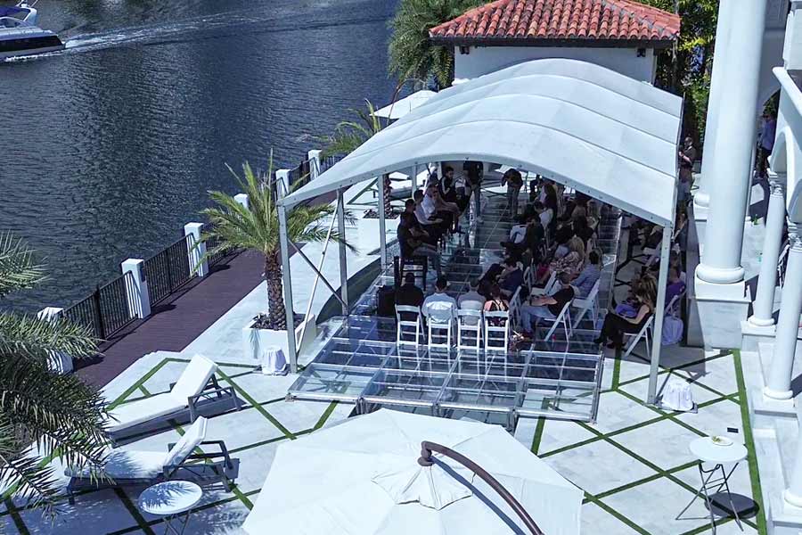 White tent with clear flooring set up on a waterfront patio with rows of chairs for a ceremony.