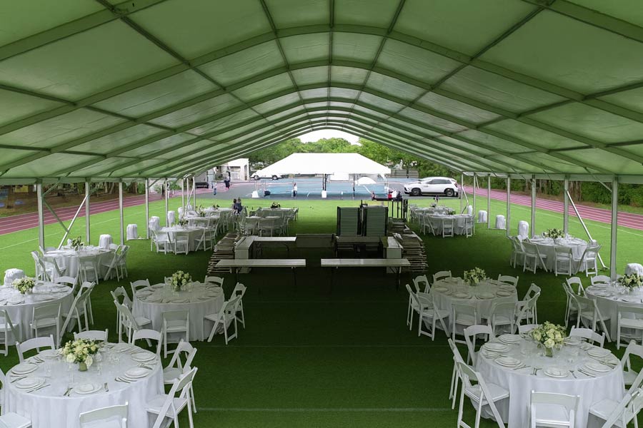 Spacious frame tent on a sports field, set up with white round tables for an elegant lounge-style event.