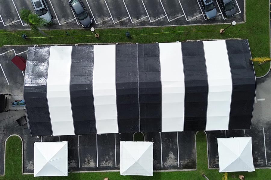 Black and white striped event tent covering a parking lot, with smaller canopy tents in the foreground.