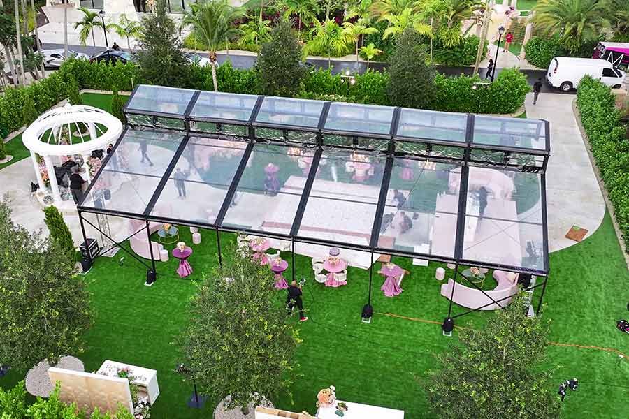 Stylish clear roof event tent with pink furniture and decorations set up on a lawn for a celebration.