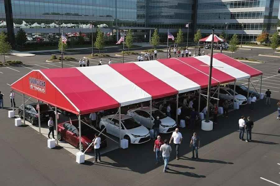 Overhead view of two long white modular tents set up on a parking area next to a building.