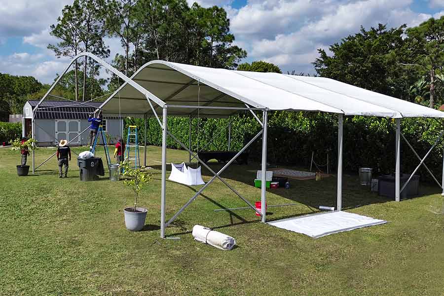 Event staff assembling a white frame tent on a backyard lawn, solving outdoor event space challenges.