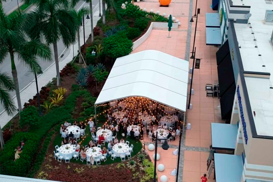 Aerial view of commercial outdoor event featuring a white tent, round dinner tables, and market buildings.