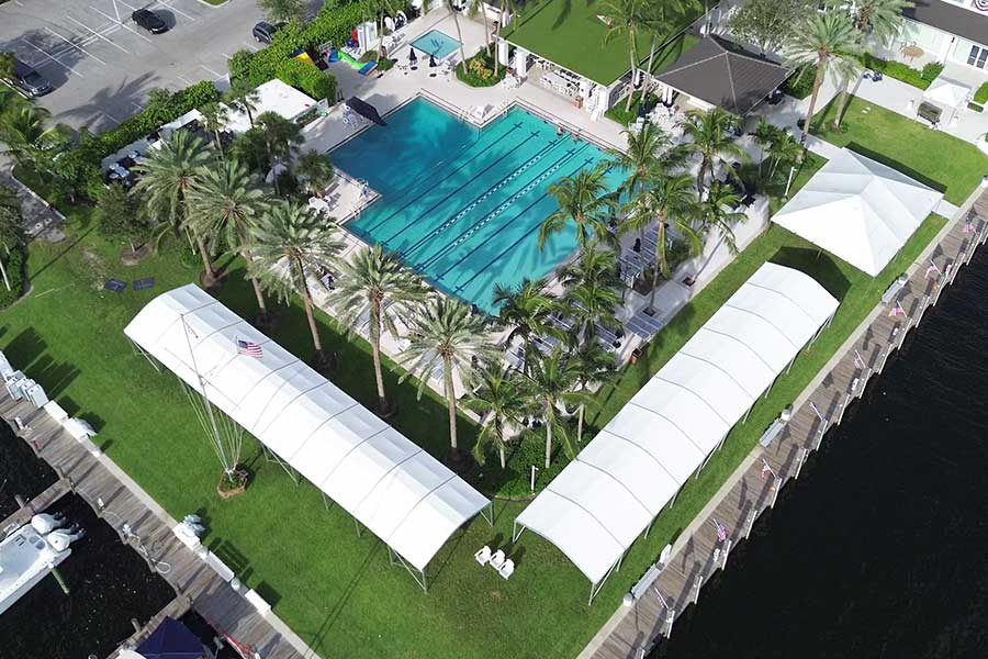 Large curved roof tents and an event marquee flanking a swimming pool and boat docks.