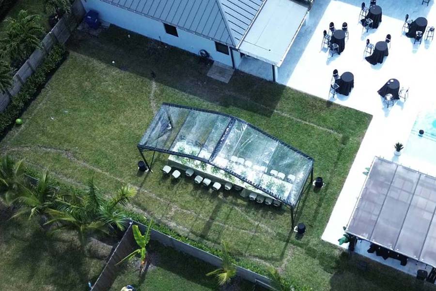 Clear curved event tent on a lawn with dinner seating; outdoor reception space near a white patio.