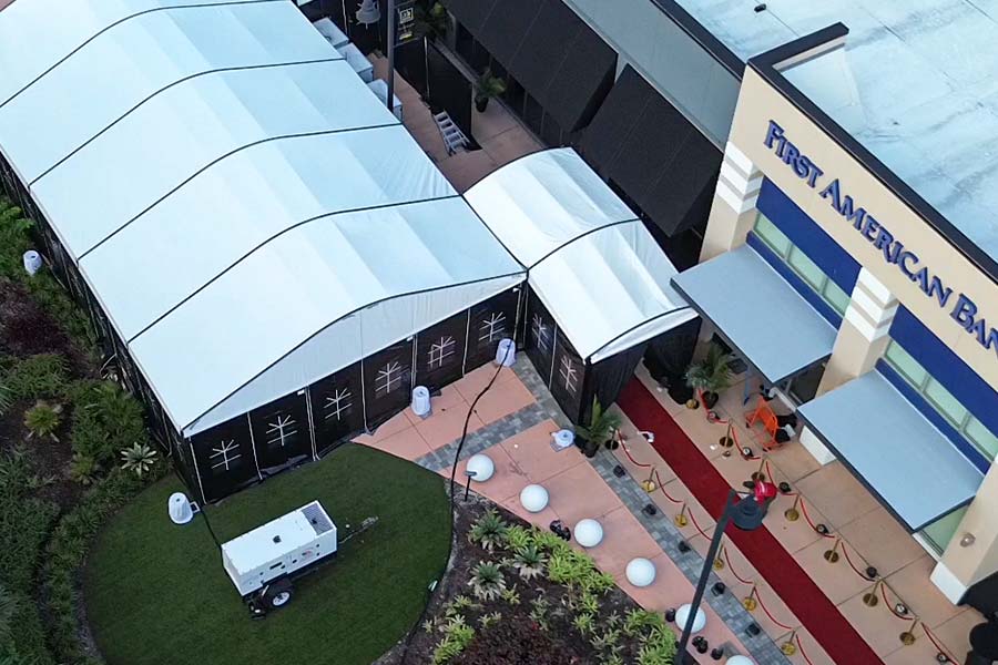 Aerial view of connected white event tents beside bank and red-carpet entrance