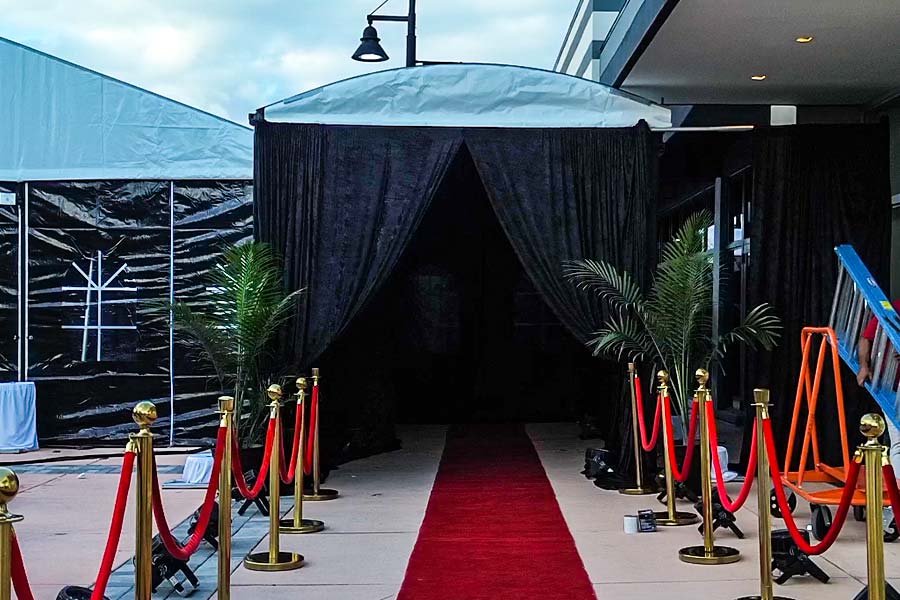 Black curtained tent entrance with red carpet and gold stanchions for VIP event