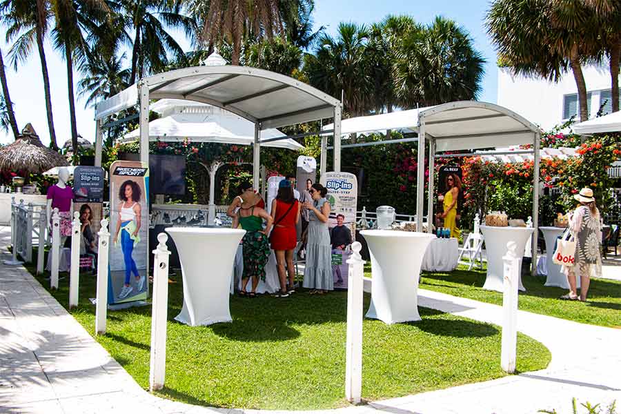 White curved tents for outdoor brand event with cocktail tables under palm trees at resort.