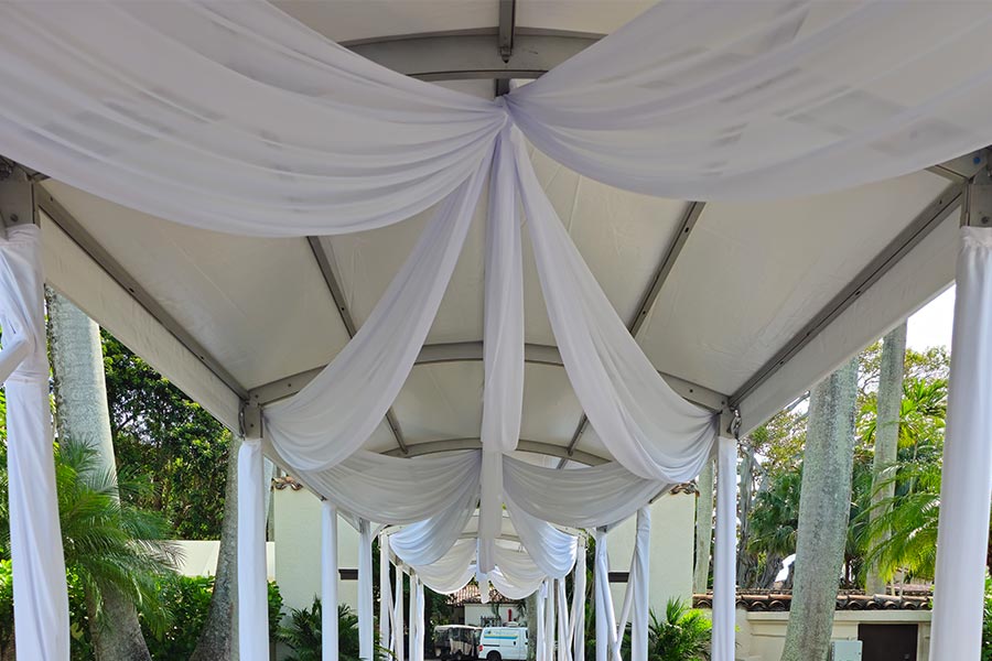Interior of white canopy walkway with white drapes creating elegant event atmosphere.